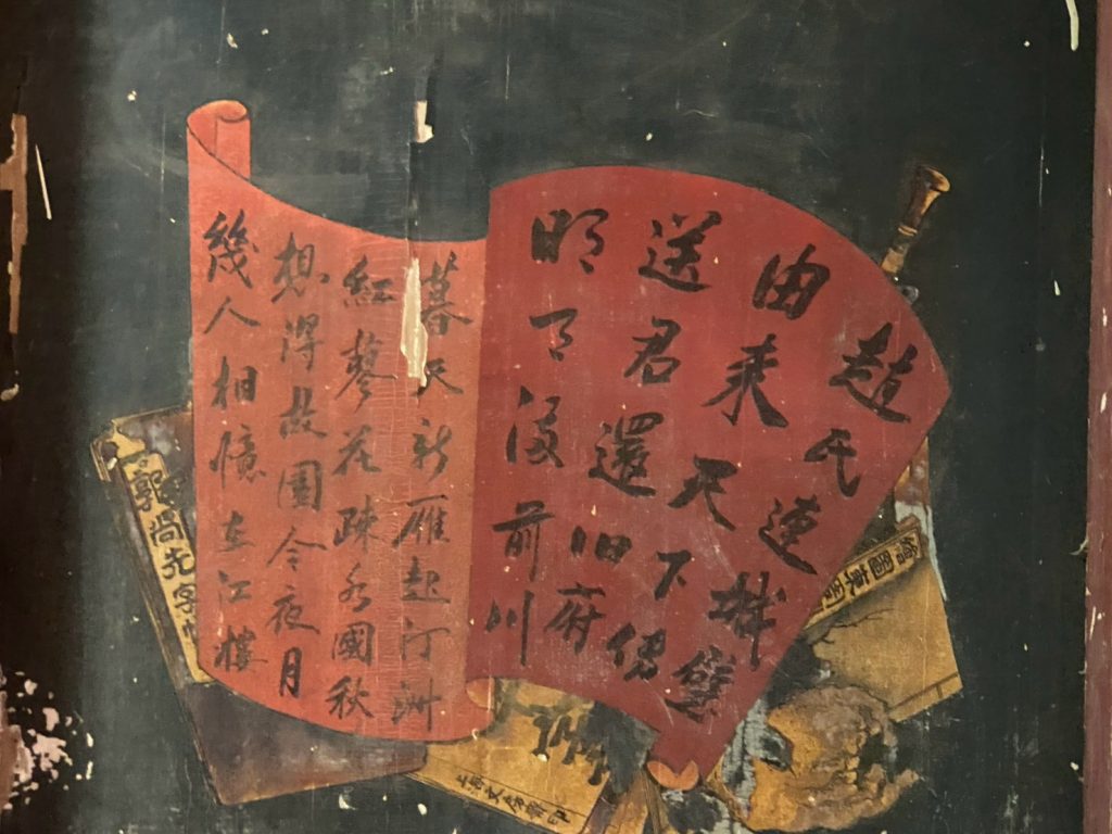 構圖精巧、詩書畫三絕的門板彩繪。匠師以疊軸展卷的立體視覺為基底，將經典唐詩以縱逸流暢的行草書寫於硃砂赤卷之上，黑底紅卷、墨韻渾厚，既有文人墨客的風雅意境，又兼具傳統民間工藝的古樸美感